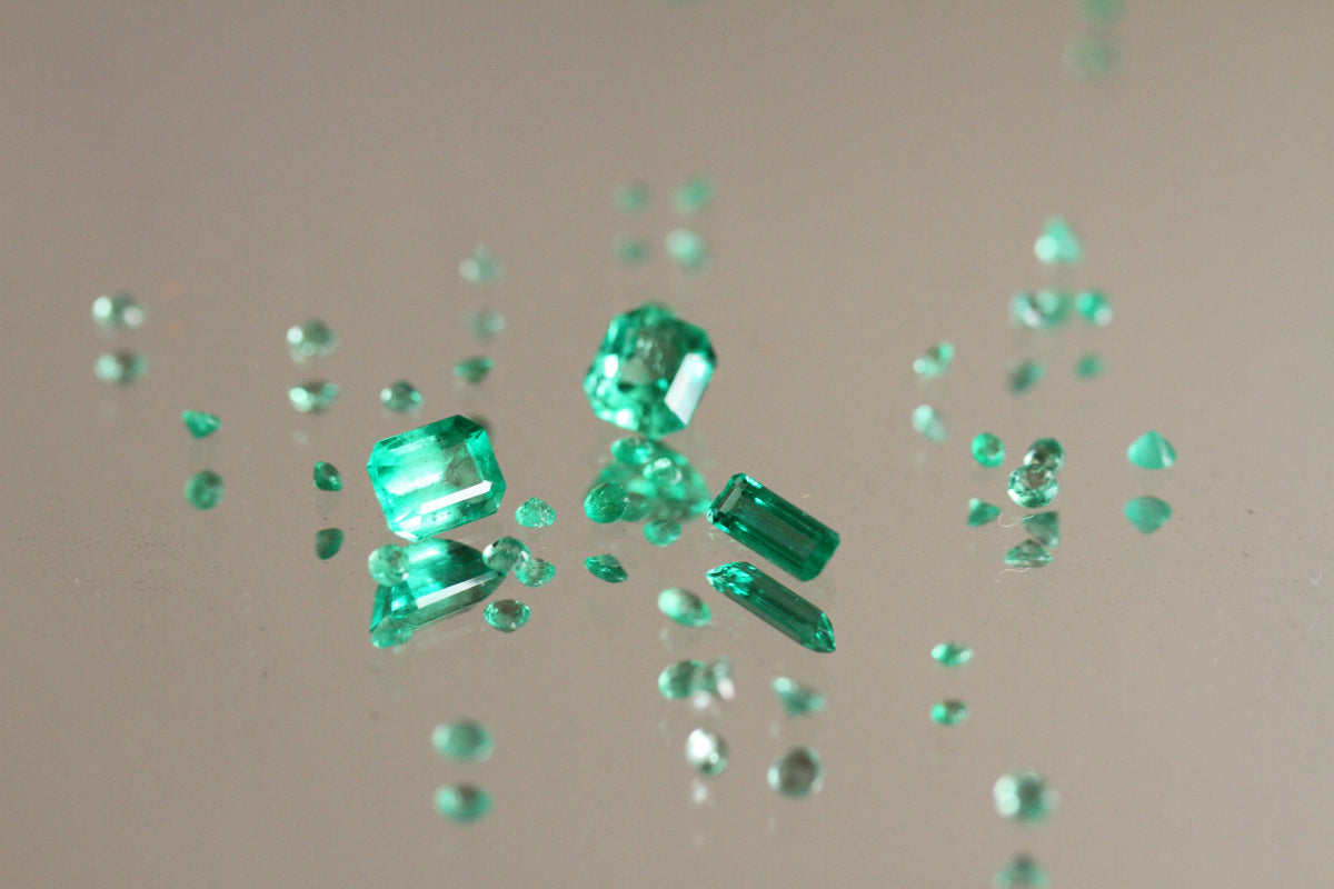 Three bright green Colombian emeralds sit scattered amongst smaller little emeralds on a neutral background