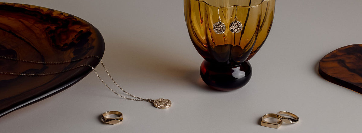 Collection of solid gold earrings, necklace and signet rings from Magpiette's Presence collection lie arranged on glassware